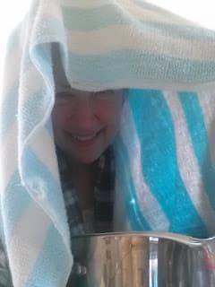 Woman with towel draped over head and steaming water pot
