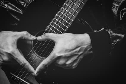 Man holding guitar making love symbol with fingers